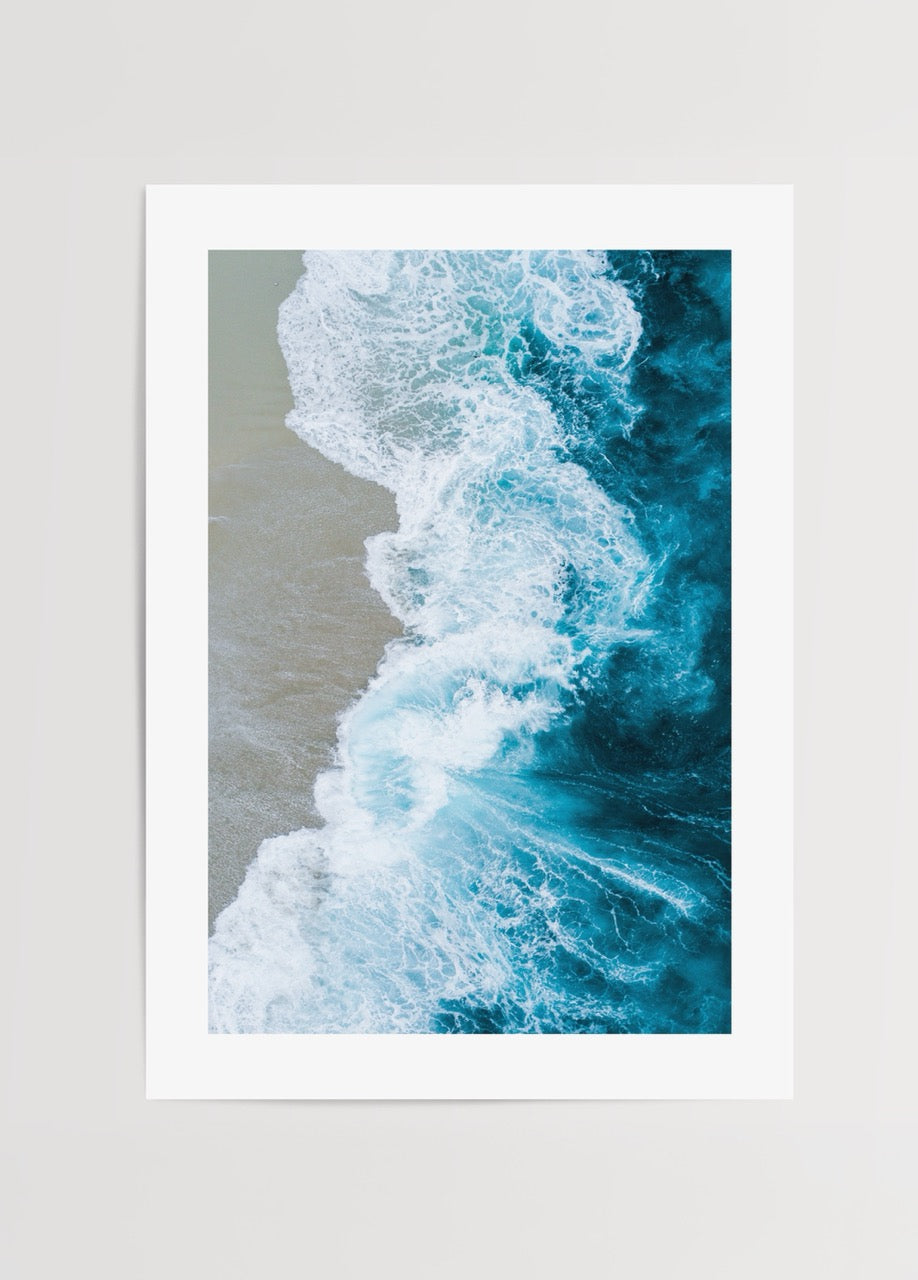 Aerial view of ocean waves merging with sandy shore in vibrant blue tones.