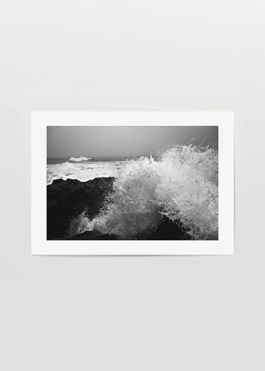 Black and white artwork of crashing waves on rocky shore