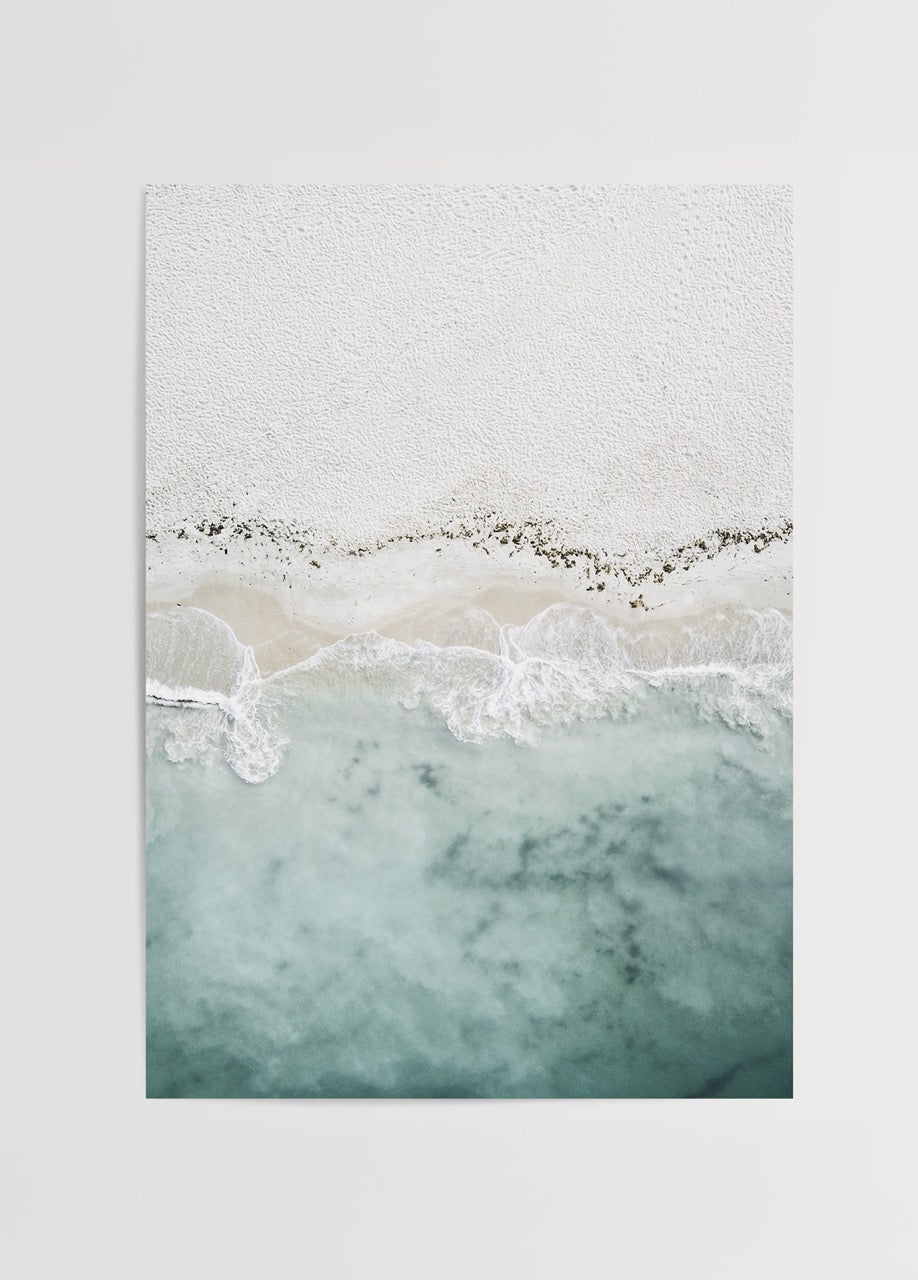Aerial view of tranquil shoreline with soft sand and blue waves.