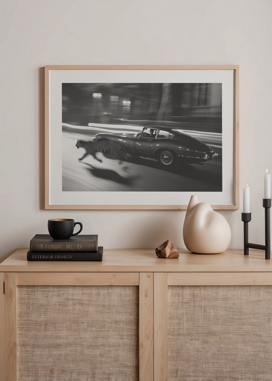 A dynamic black and white artwork featuring a leopard running alongside a vintage car.