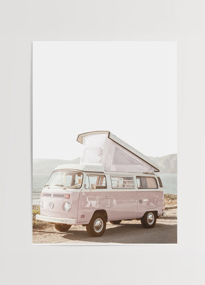 A whimsical pink caravan parked by the water, evoking adventure and nostalgia.