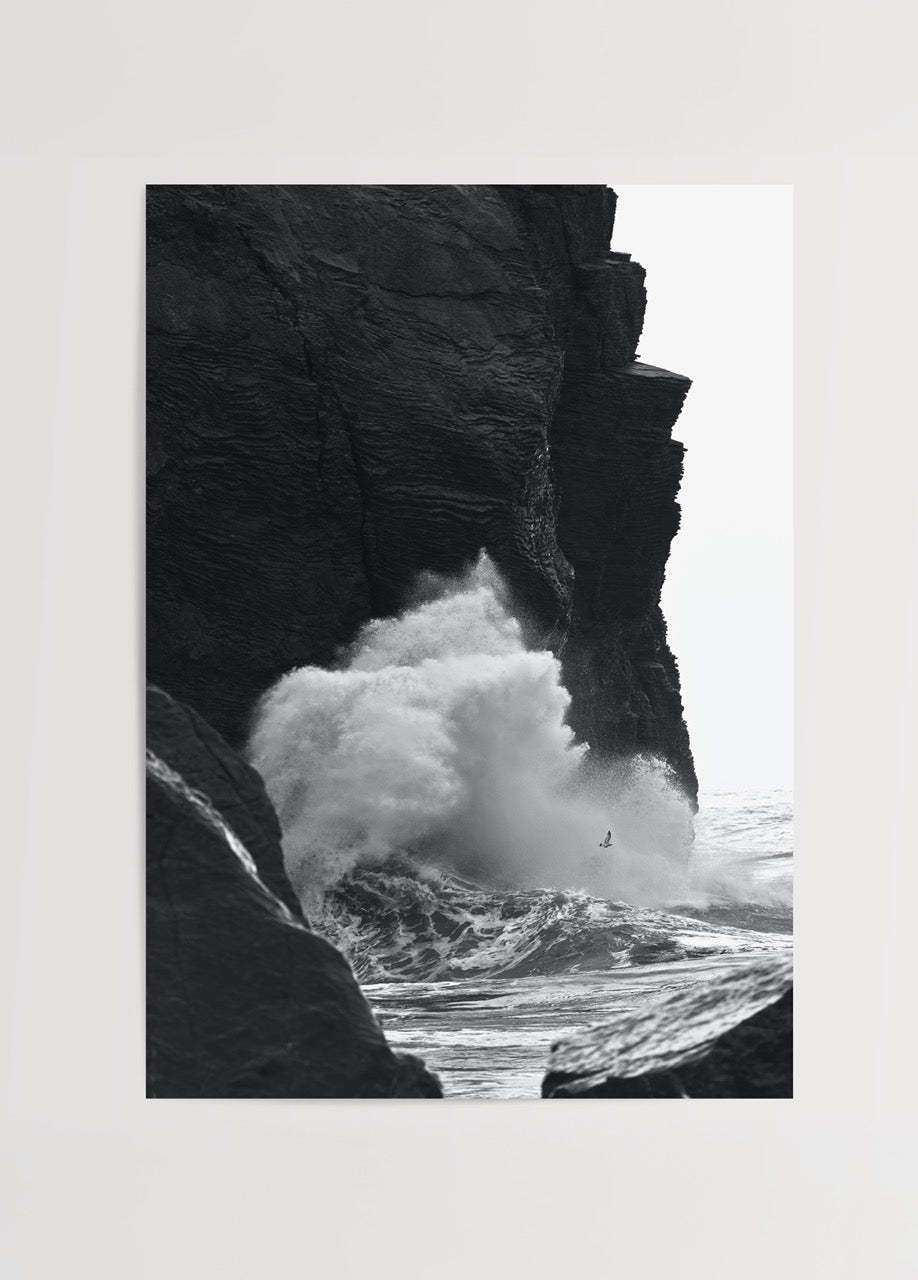 Black and white artwork of crashing waves against rocky cliffs.