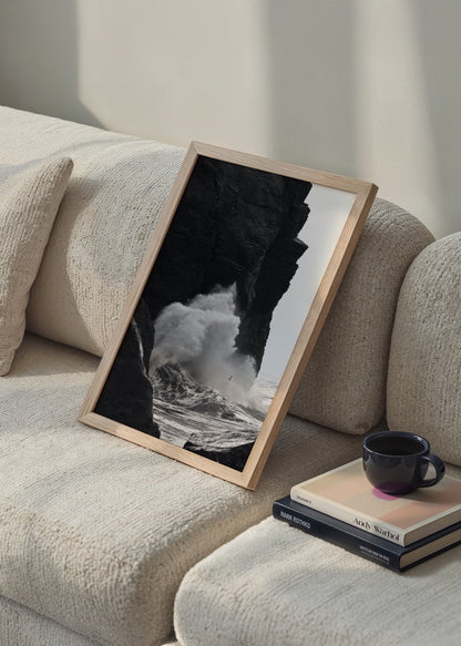 Black and white artwork of crashing waves against rocky cliffs.